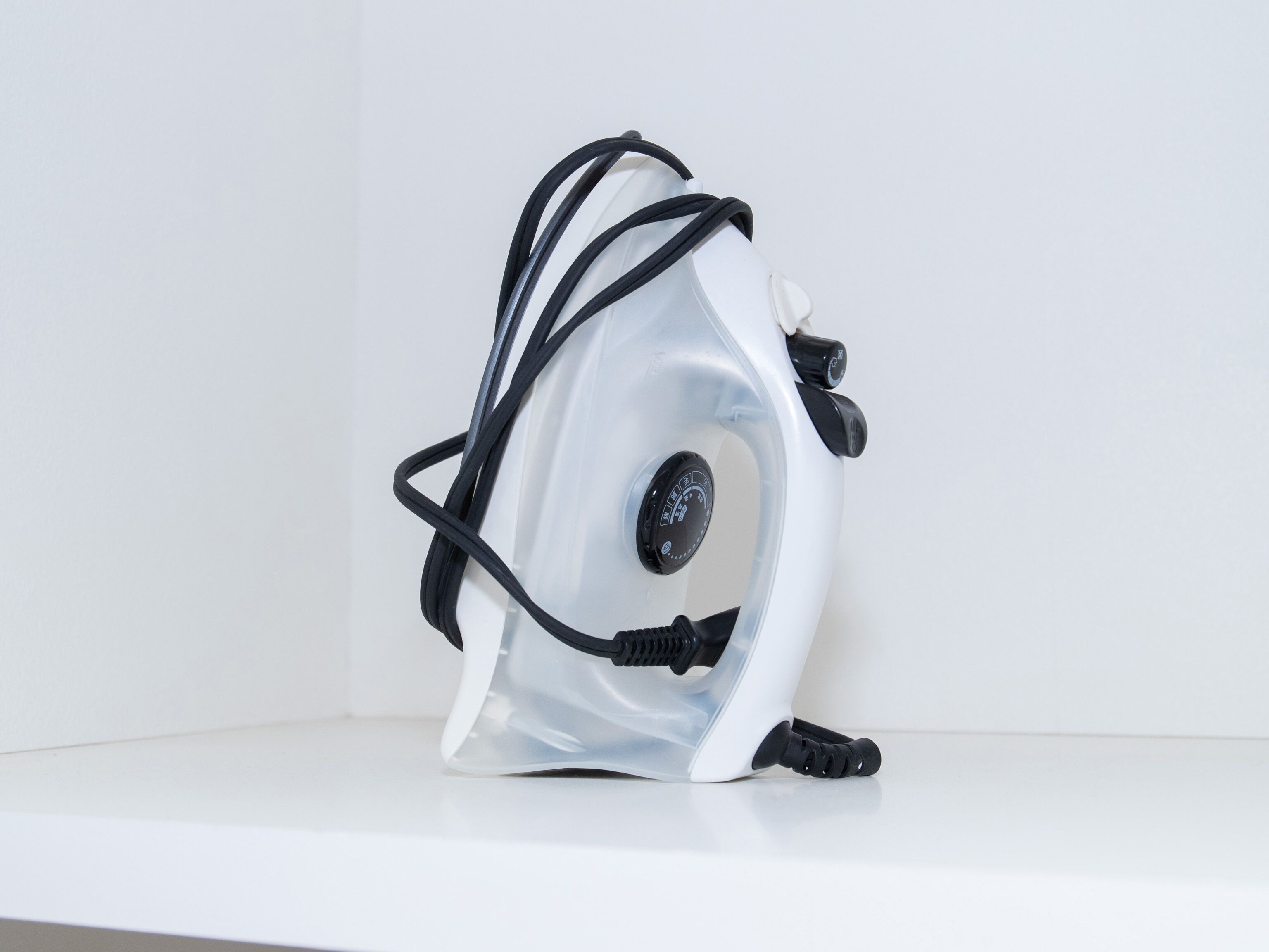 A white, transparent, and curved object with a black control panel and cables, placed on a white surface against a white background.