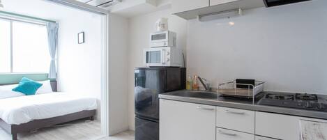A modern hotel room with a bed, a kitchenette, and a window with curtains.