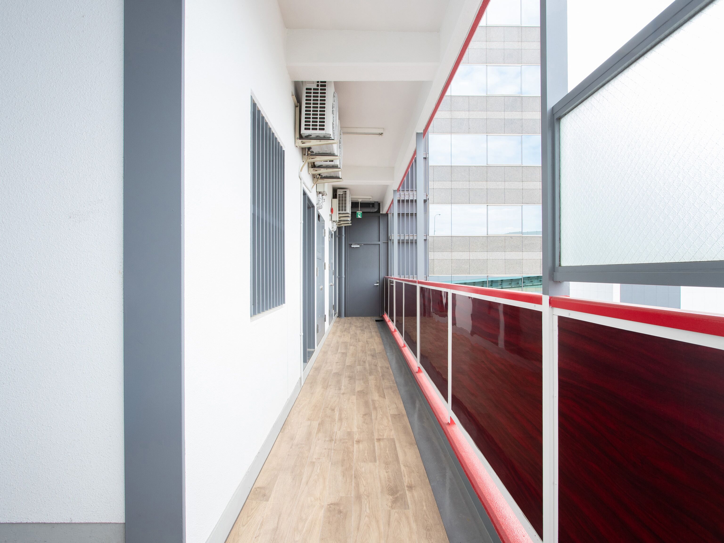 A corridor with a wooden floor, grey walls, and red railings.