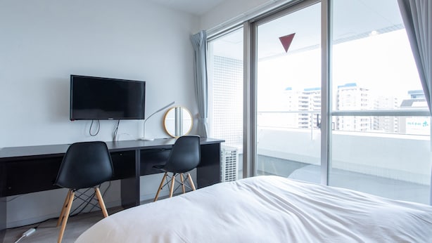 Quarto de hotel moderno com uma cama grande, uma escrivaninha com TV de tela plana, uma cadeira e uma janela ampla com vista para a cidade.