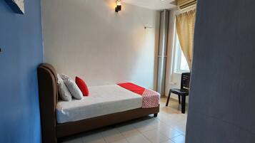 Un dormitorio con una cama, almohadas, una colcha roja, una silla y una ventana con cortinas.