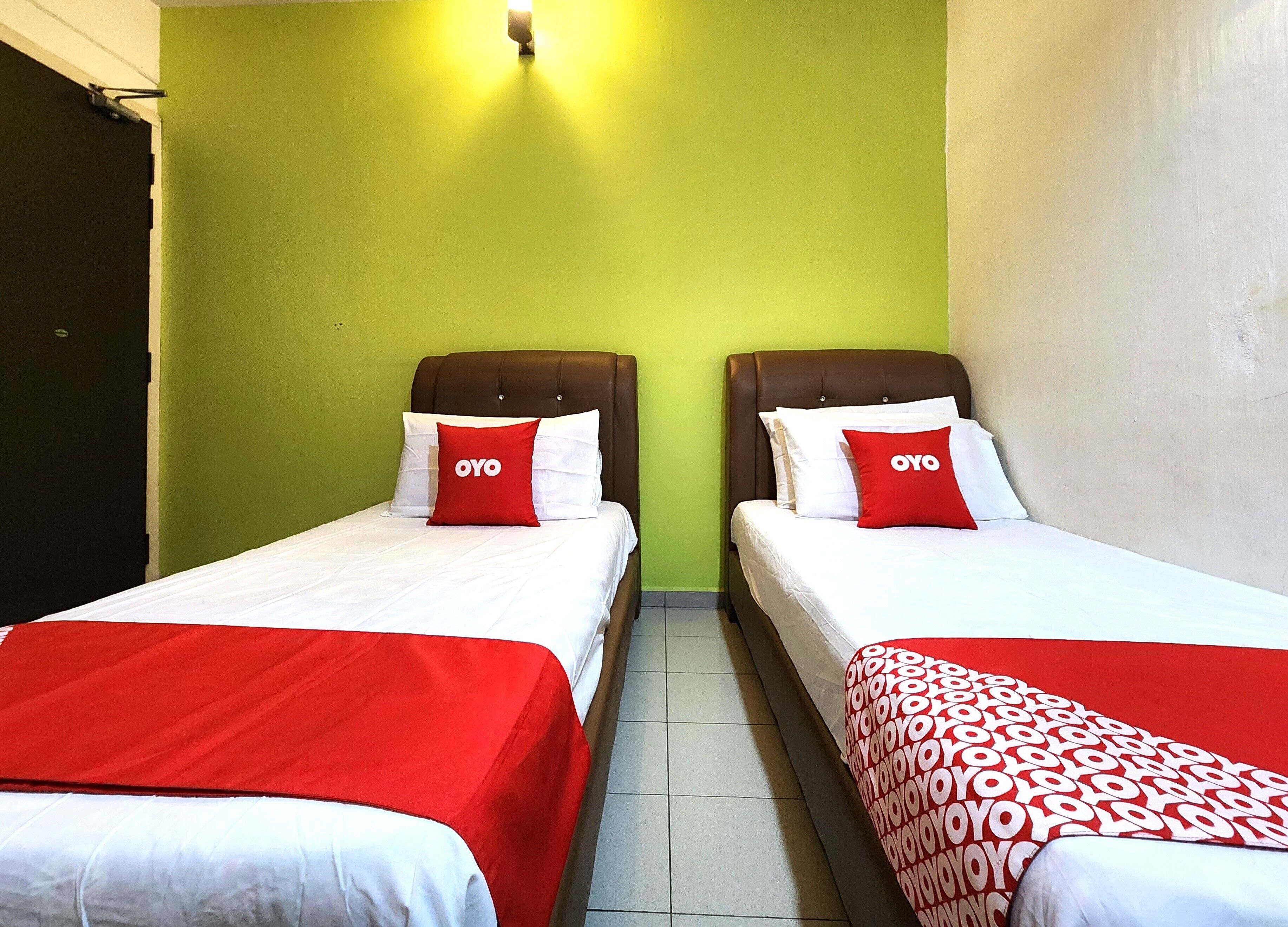 Dos camas individuales con ropa de cama roja y blanca, una pared verde y una lámpara sobre las camas.
