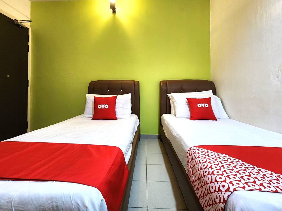 Dos camas individuales con ropa de cama roja y blanca, una pared verde y una lámpara sobre las camas.