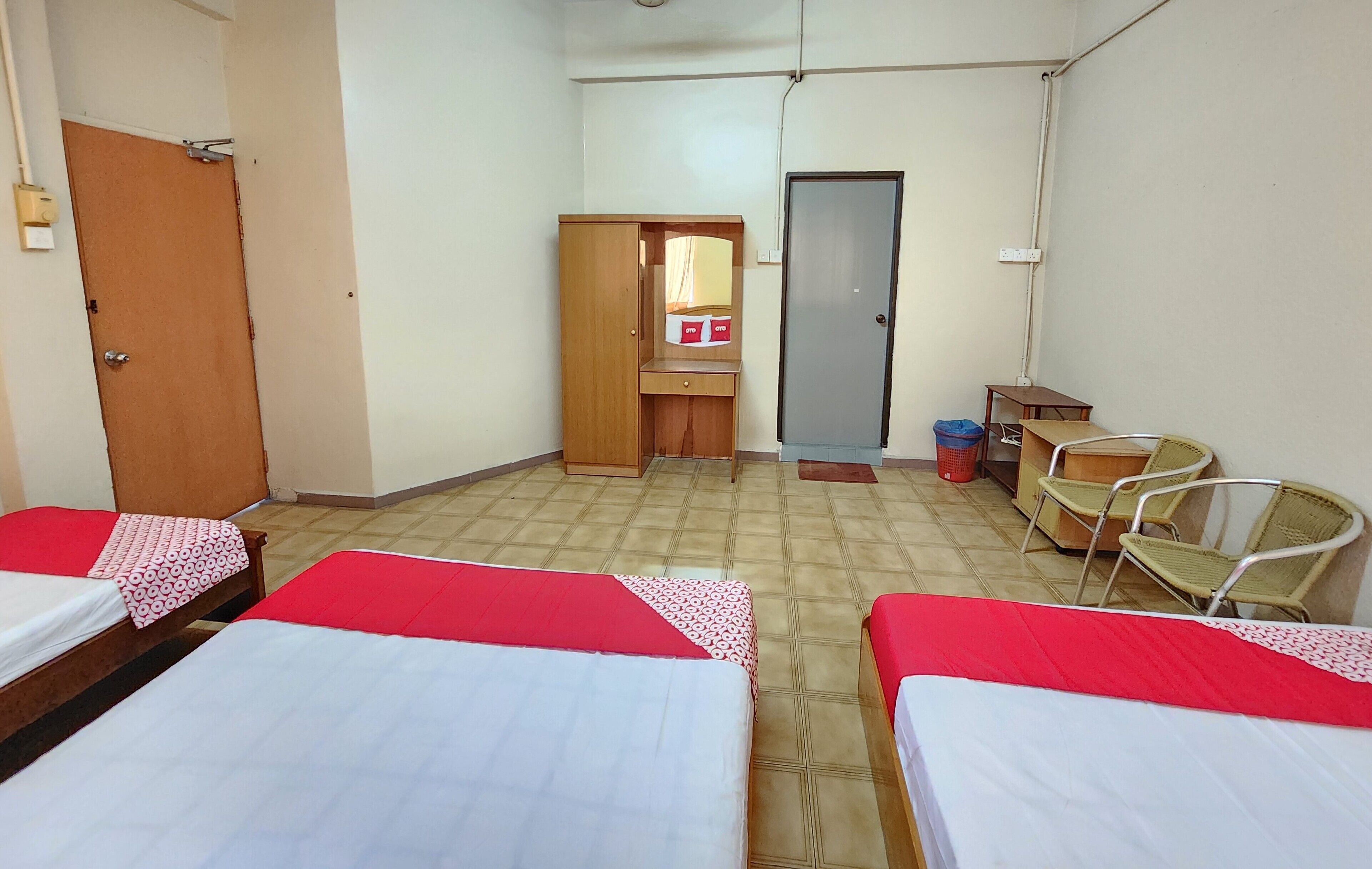 A room with three beds, a wooden wardrobe, a small desk, and a mirror.