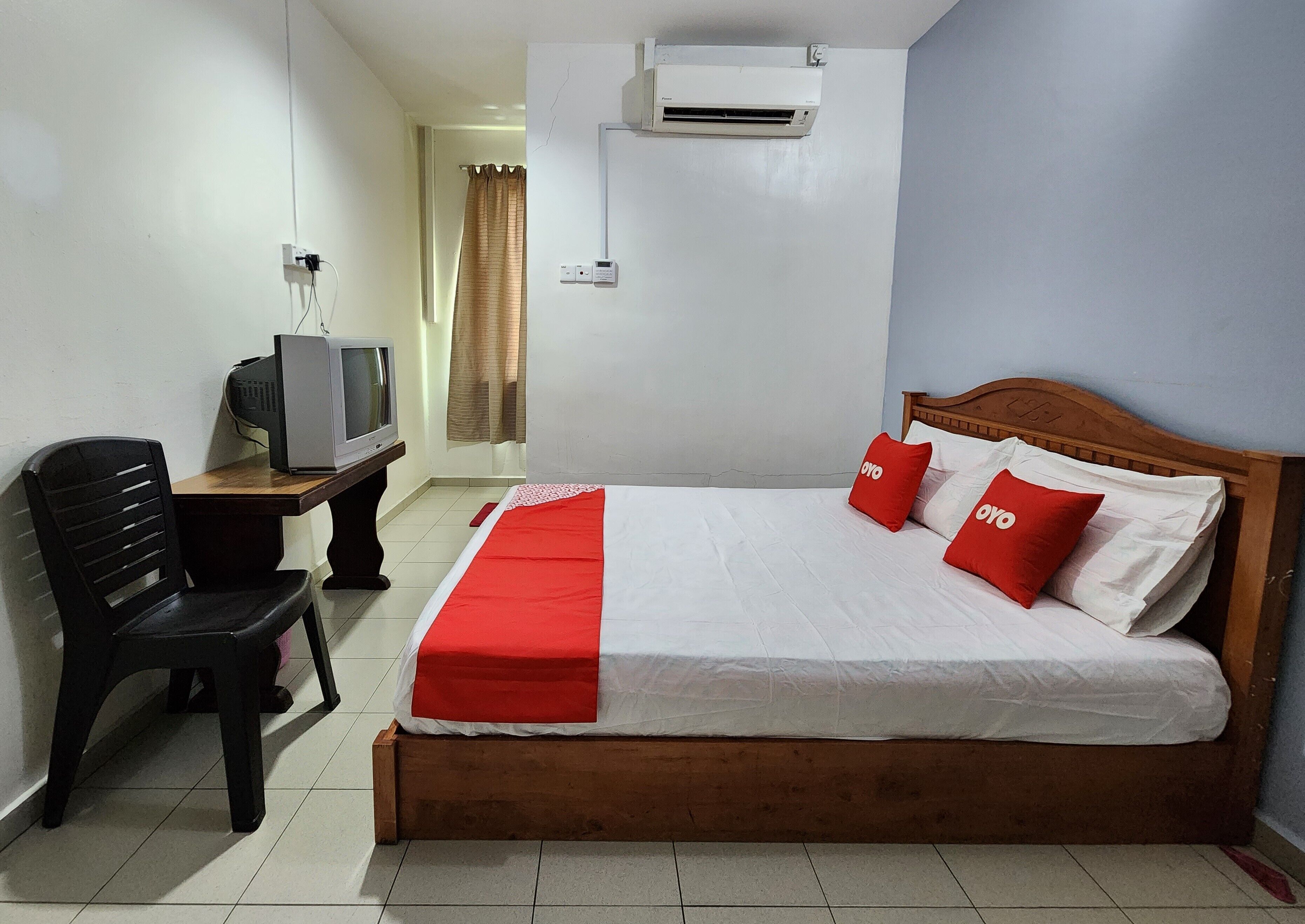 A hotel room with a wooden bed, a television on a desk, and an air conditioning unit on the wall.