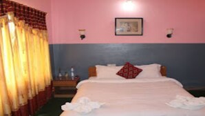 Una habitación de hotel con cama, cortinas, mesita de noche y un cuadro colgado en la pared.