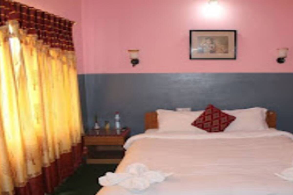 A hotel room with a bed, curtains, a nightstand, and a wall-mounted picture.