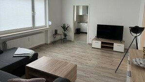 En moderne stue med sofa, sofabord, fjernsyn og et lille spiseområde.