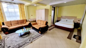 Een hotelkamer met een bank, een bed, een glazen bijzettafeltje en een kamerkleed met een patroon.