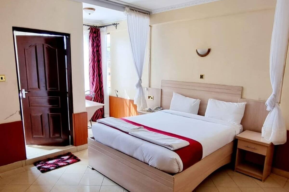 Una habitación de hotel con una cama, mesitas de noche, una puerta y piso de baldosas.
