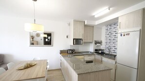 Une cuisine moderne dotée d’un îlot central, de meubles blancs, d’un four à micro-ondes et d’un réfrigérateur.