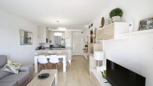 Un salon moderne avec un canapé gris, une table basse, un téléviseur et un coin repas comprenant des chaises et une table.