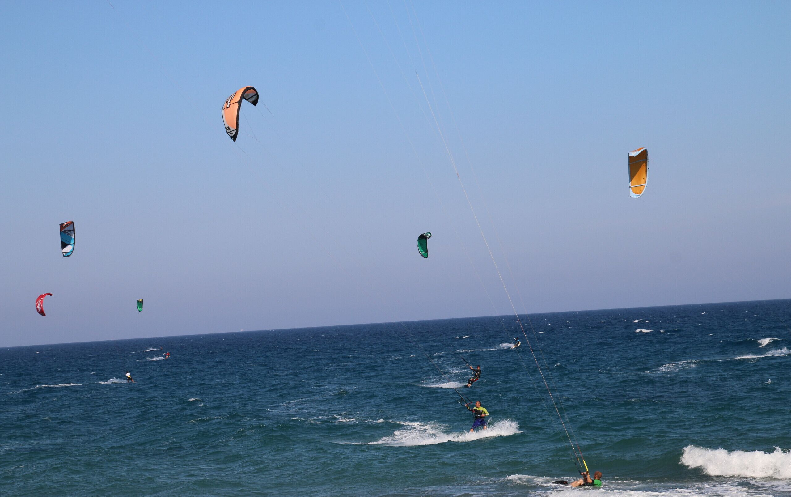 Una playa con varios kitesurfistas y cometas volando.