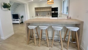 Una cocina moderna con una isla central, taburetes de bar, una lámpara colgante y vistas a una escalera que lleva a una zona de estar.