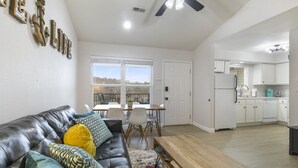 A modern living room with a leather sofa, a wooden coffee table, and a dining area with a white table and chairs. A kitchen with white cabinets and appliances is visible in the background. - Lighthouse Retreat – Pool, Swim Dock and More! (Lake Ozark)
