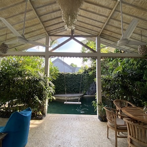 A covered outdoor area with a pool, seating, and lush greenery.