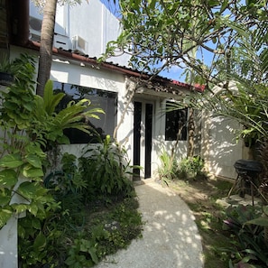 Stroll through lush gardens to the entrance of this charming building, featuring a white facade and red-tiled roof.