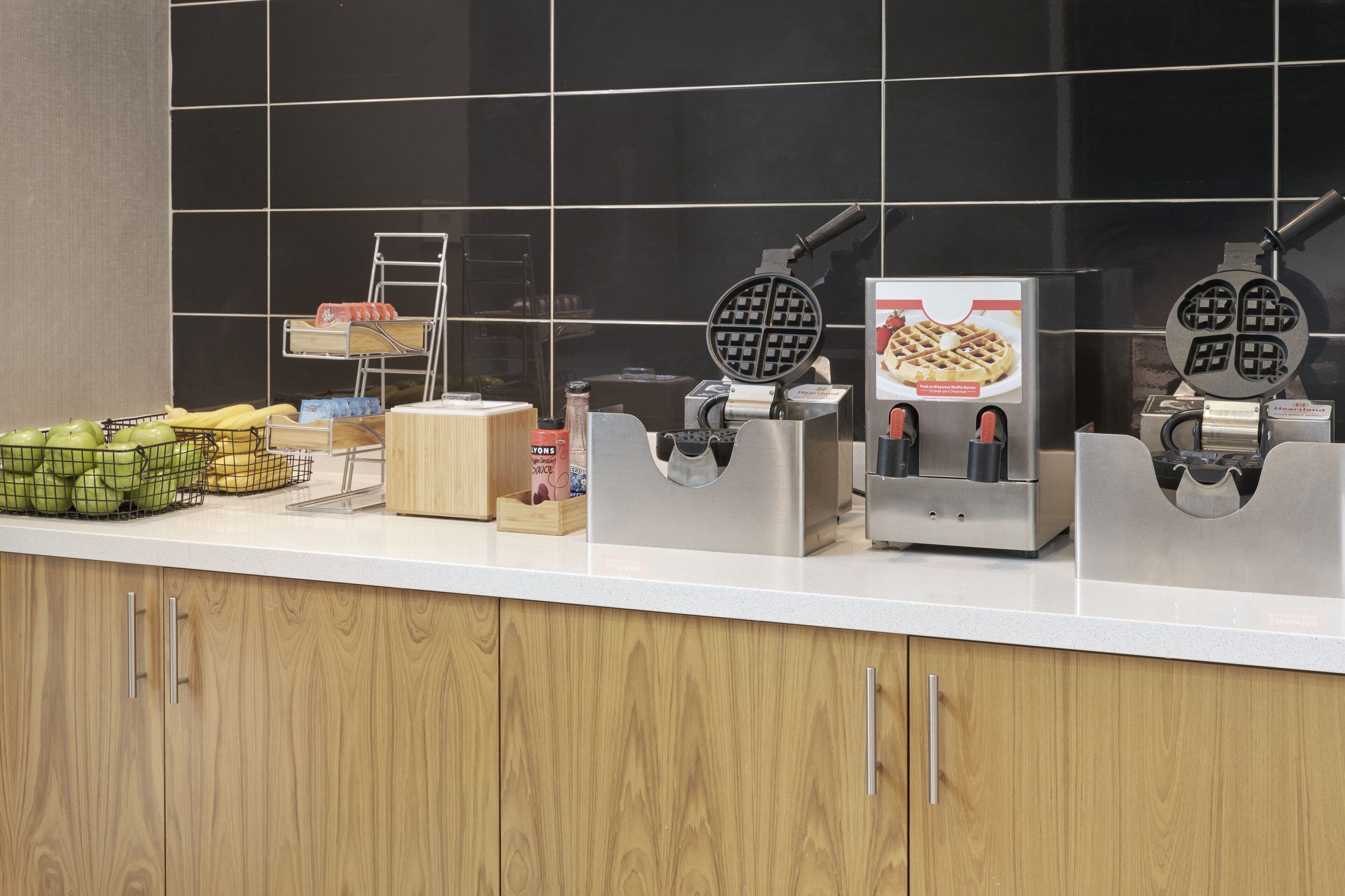A kitchen counter with waffle makers, a fruit basket, and a coffee machine.