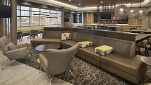 Un hall d’hôtel moderne avec un canapé d’angle, des tables rondes et un coin bar.
