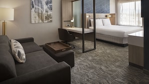 Une chambre d’hôtel avec un lit, un bureau, une chaise, un canapé et une lampe.