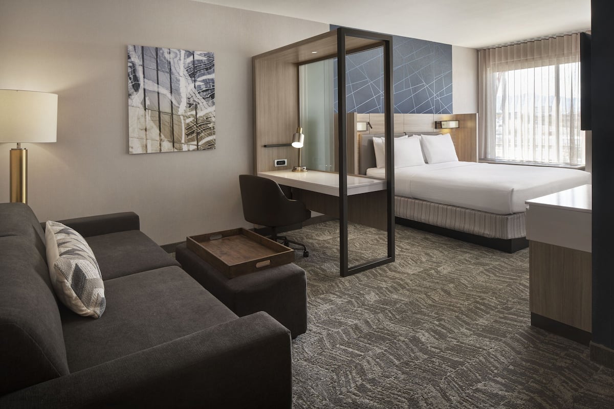 Une chambre d’hôtel avec un lit, un bureau, une chaise, un canapé et une lampe.