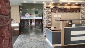 Zona de recepción con un fondo de pared de piedra, un mostrador de madera y un letrero que dice 'TAMA SUSHI'.