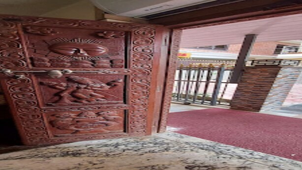 Una puerta de madera con intrincados grabados, un portón de metal y una alfombra roja que conduce al exterior.