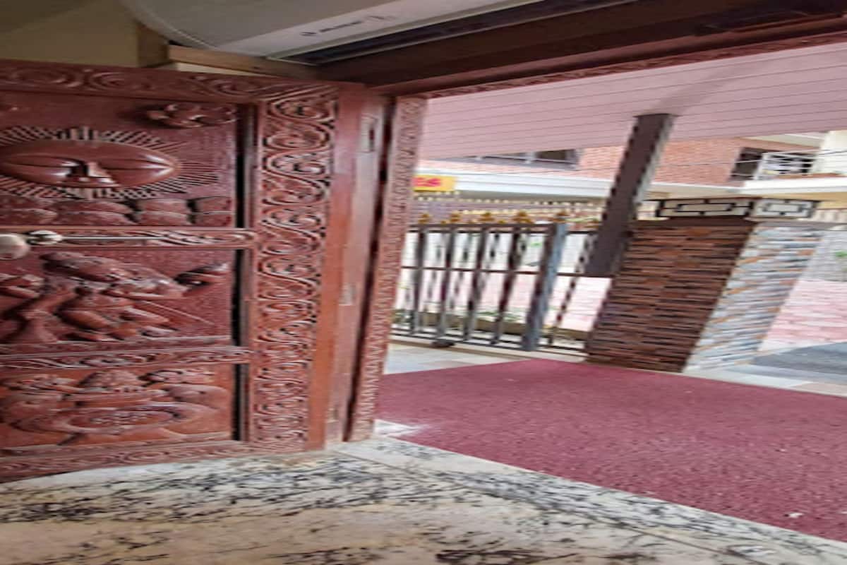 Una puerta de madera con intrincados grabados, un portón de metal y una alfombra roja que conduce al exterior.
