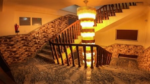 Una escalera con barandilla de madera, pared con diseño y candelabro.