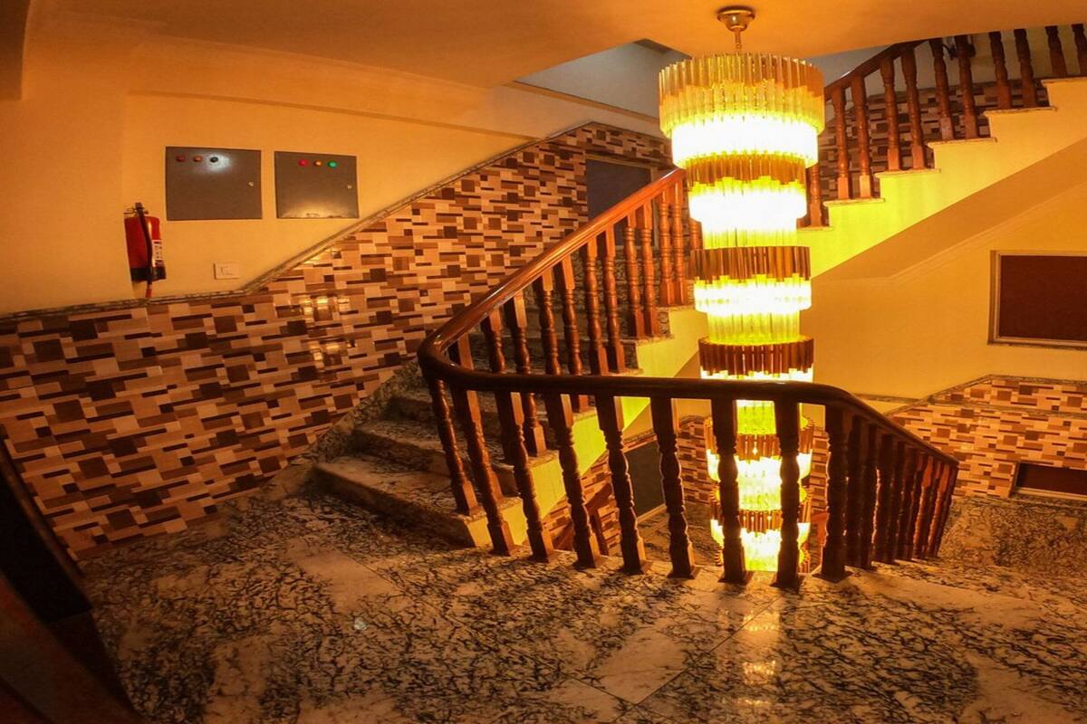 Una escalera con barandilla de madera, pared con diseño y candelabro.