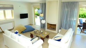 A living room with white sofas, a coffee table, a fireplace, and a television on the wall. - Citron Pale Villa with Private Pool (Trifylia)