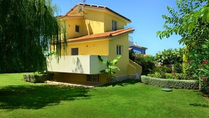 A two-story yellow building with a red-tiled roof, surrounded by well-maintained green lawns and various plants. - Citron Pale Villa with Private Pool (Trifylia)