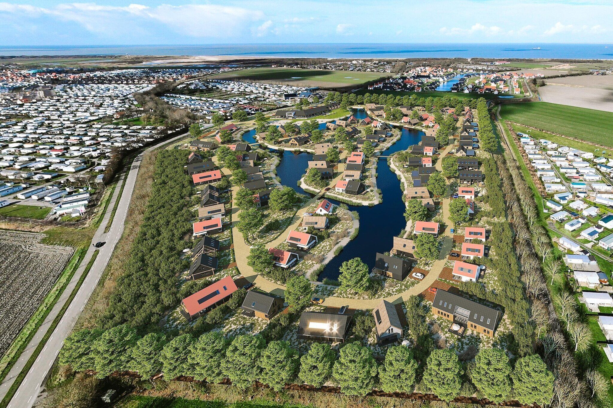An aerial view of a residential area with houses, a river, and a beach in the background.