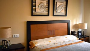 A hotel room with a large bed, a nightstand with a lamp, and two framed artworks on the wall.