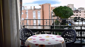 A balcony with a table and chairs, a potted plant, and a view of buildings in the background.