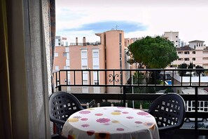 A balcony with a table and chairs, overlooking a residential area with buildings and a tree.