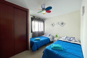 A room with two beds, a ceiling fan, a window with curtains, and wall art.