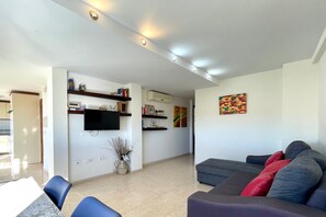 A modern living room with a sofa, a flat-screen TV, and a dining area with chairs.