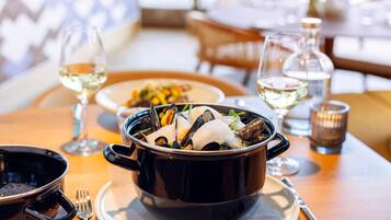 A dining table with a black pot of seafood, a glass of white wine, and a candle.