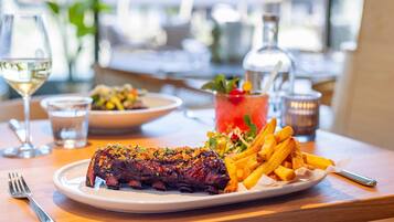 A dining table with a plate of steak and fries, a glass of white wine, and a cocktail with a garnish.