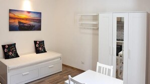 A room with a white sofa, a dining table, a white wardrobe, and a painting of a sunset over a pier.