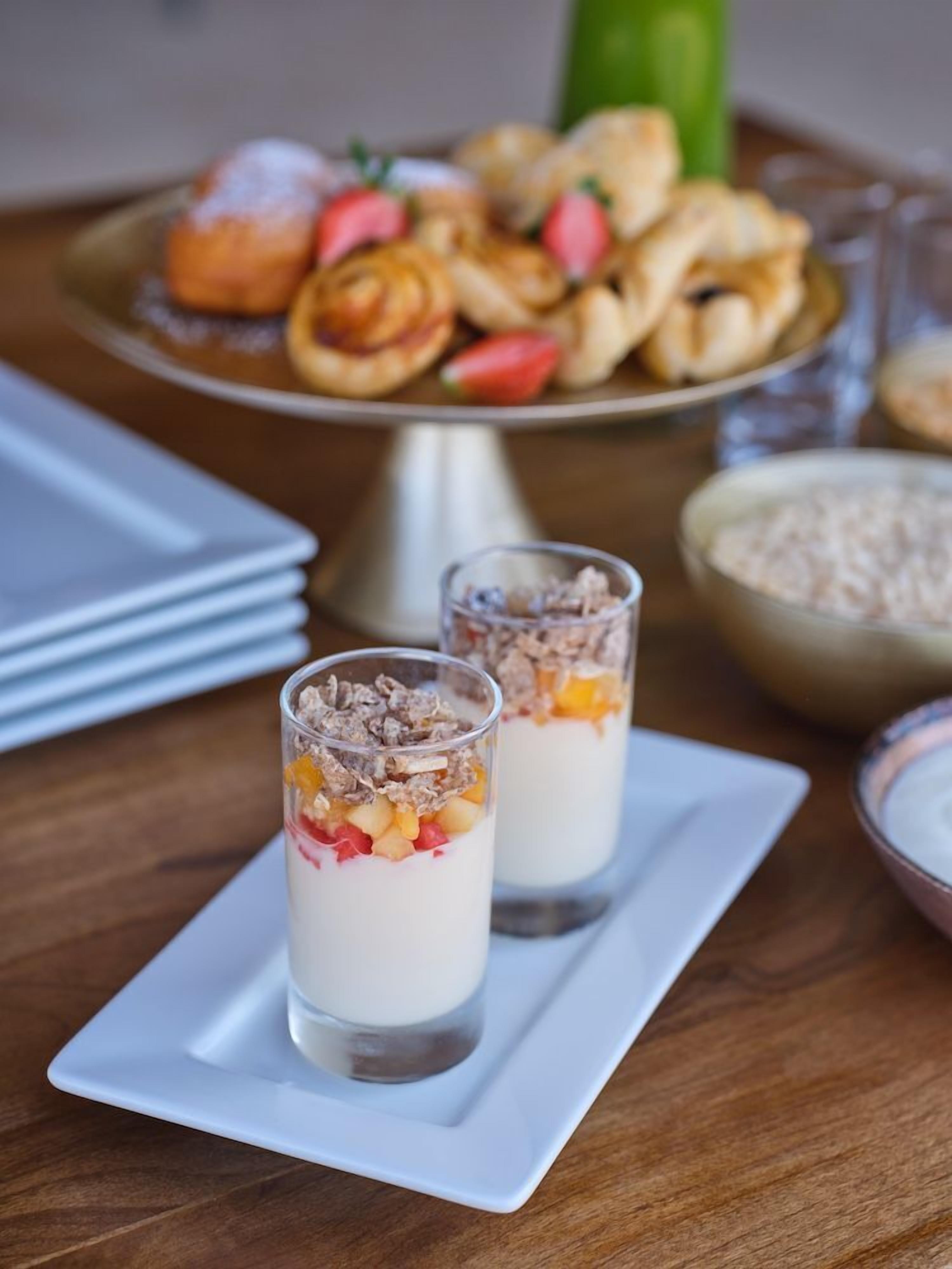 Two glasses of layered dessert with a plate of pastries in the background.