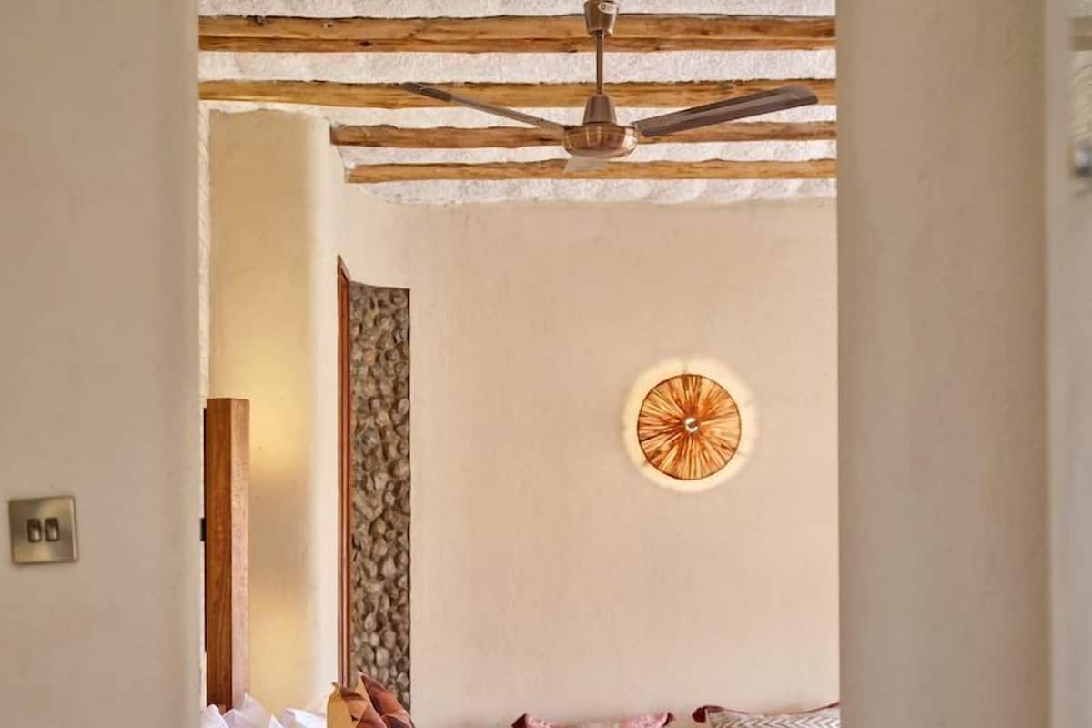 Un dormitorio con una cama, una planta en maceta, un reloj de pared y un ventilador de techo.