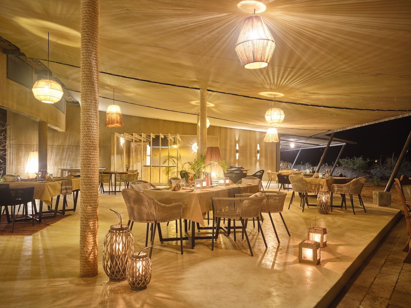 An outdoor dining area with round tables and chairs, ambient lighting, and decorative lanterns.