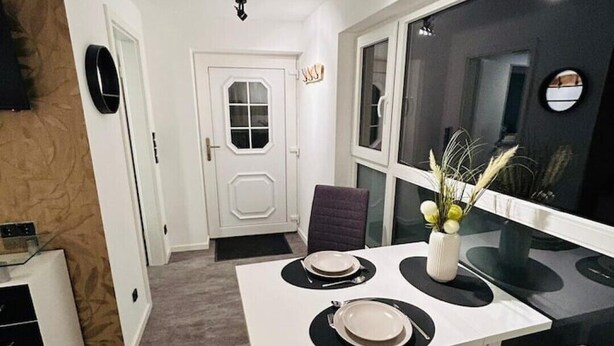 A compact dining area with a white table set for two, a modern kitchen with black countertops, and a large window with a view. - Charming apartment in the heart of Nieukerk. (Kerken)