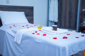 A neatly made bed with white linens, a bottle of lotion, and scattered rose petals. - Kisimani Eco Resort & Spa (Isiolo)