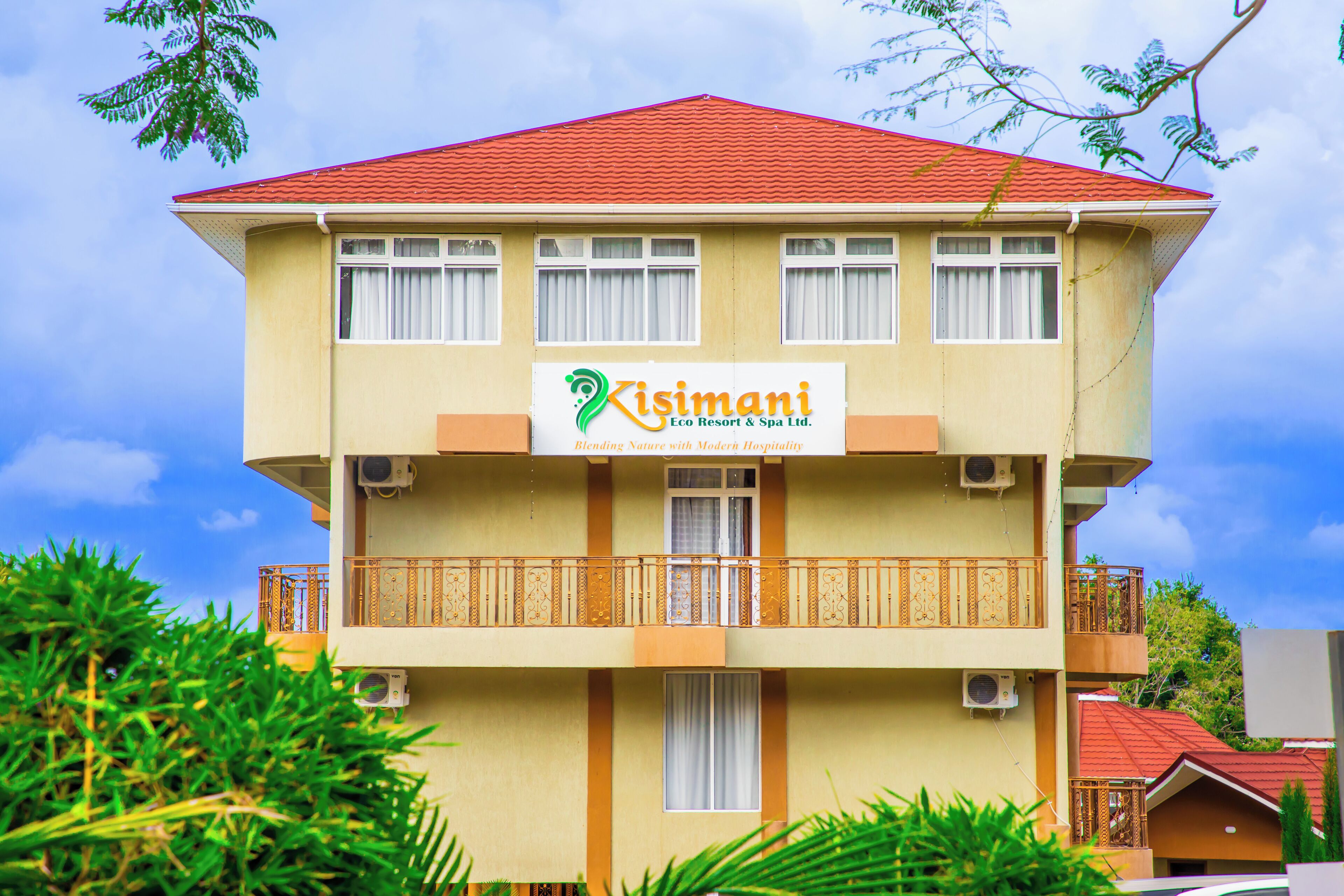 Un bâtiment à deux étages, sur lequel on peut lire l’enseigne « Kisimani Eco Resort & Spa Ltd. », doté de balcons avec des garde-corps en bois et de climatiseurs.