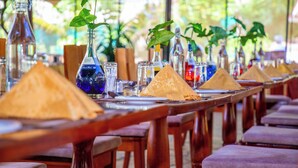 Un restaurante con mesas y sillas de madera, botellas de vidrio y servilletas con forma de pirámide.