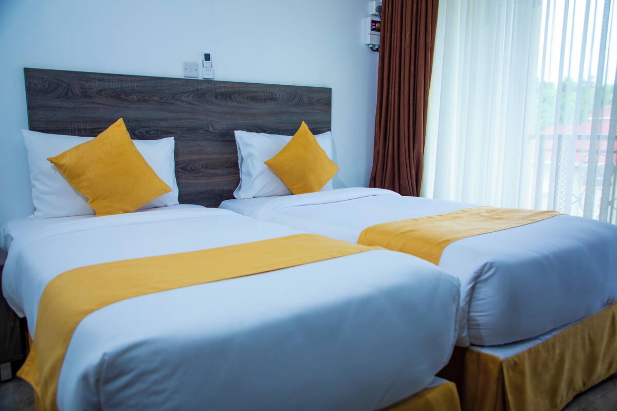 Ein Hotelzimmer mit zwei Betten, jeweils mit weißer Bettwäsche und einem gelben Zierkissen.