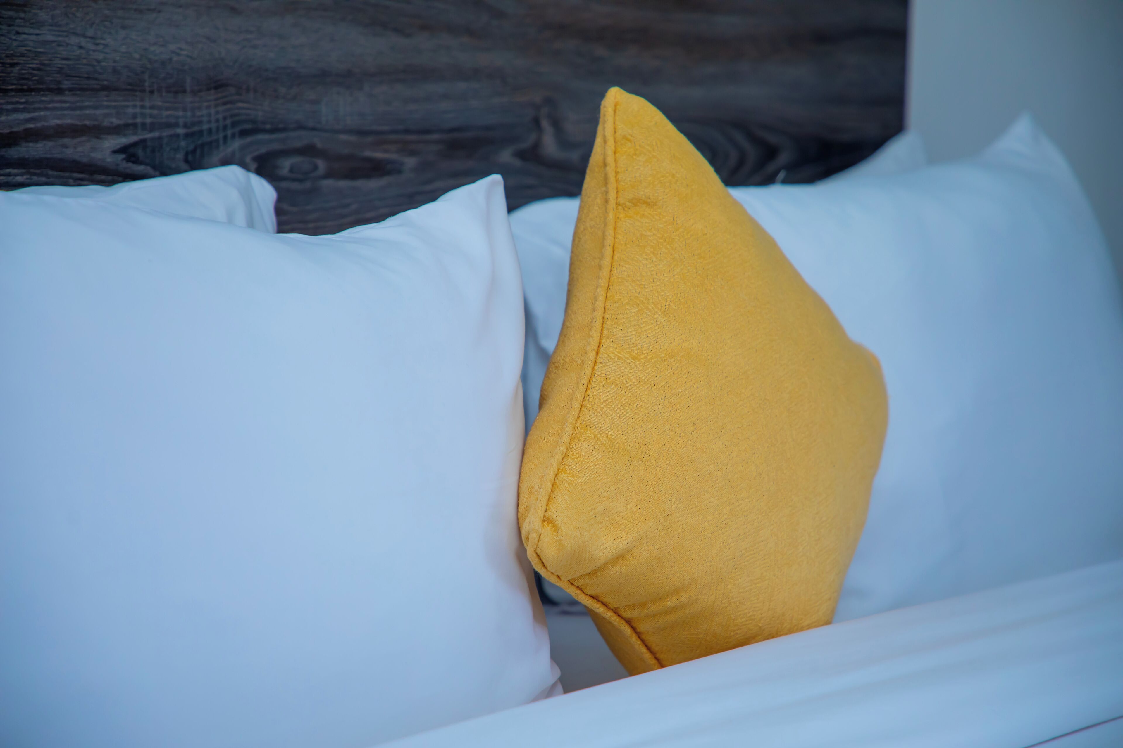Een bed met witte lakens en één mosterdgeel kussen.